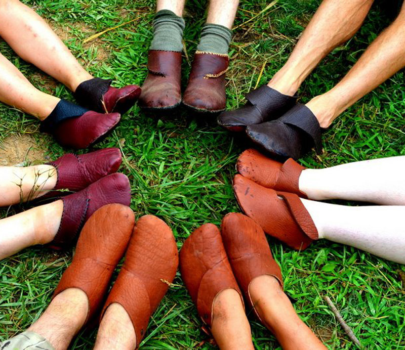 Closeup of feet of people wearing handmade shoes lying in a circle with feet pointed inward creating a circle of shoes