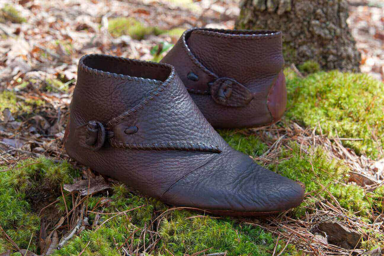 Dark pair of leather shoes made at workshop displayed on moss in forest